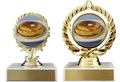 Two gold trophy cups with oval medallions showing a stack of pancakes, mounted on white bases with gold front plates, photographed on a white background.