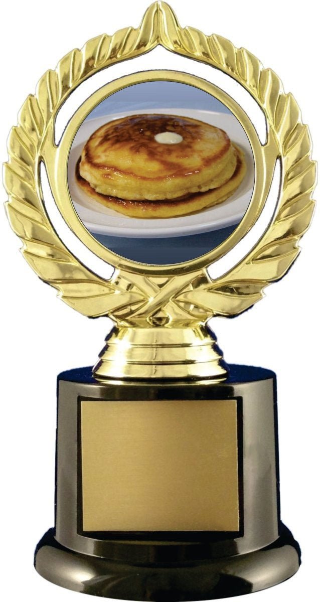 A novelty trophy with a gold-plated laurel wreath frame displaying a photo of a stack of pancakes, mounted on a black and gold base with a blank gold plaque.